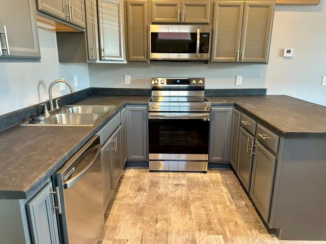 kitchen with sink, kitchen peninsula, stainless steel appliances, and light hardwood / wood-style flooring