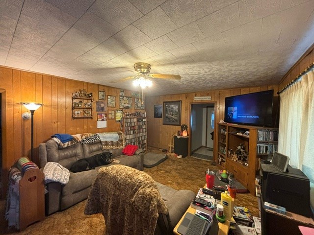 living room with ceiling fan, wooden walls, and carpet floors