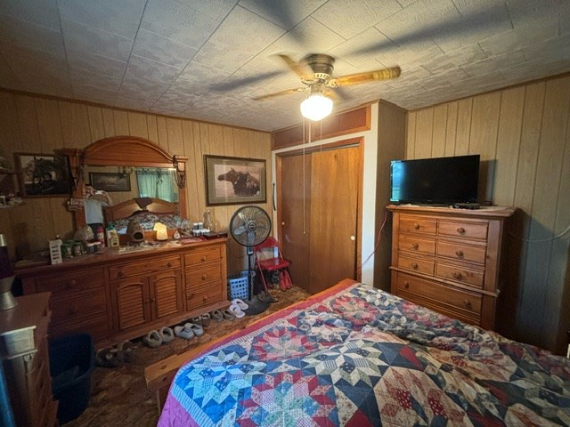 bedroom with ceiling fan, wooden walls, and a closet