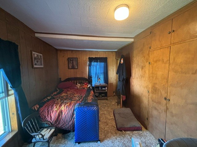 carpeted bedroom with wooden walls and a textured ceiling