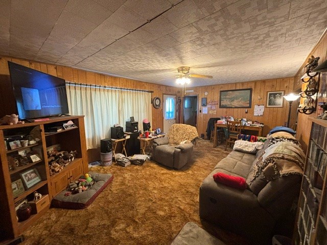 living room with wooden walls, carpet, and ceiling fan