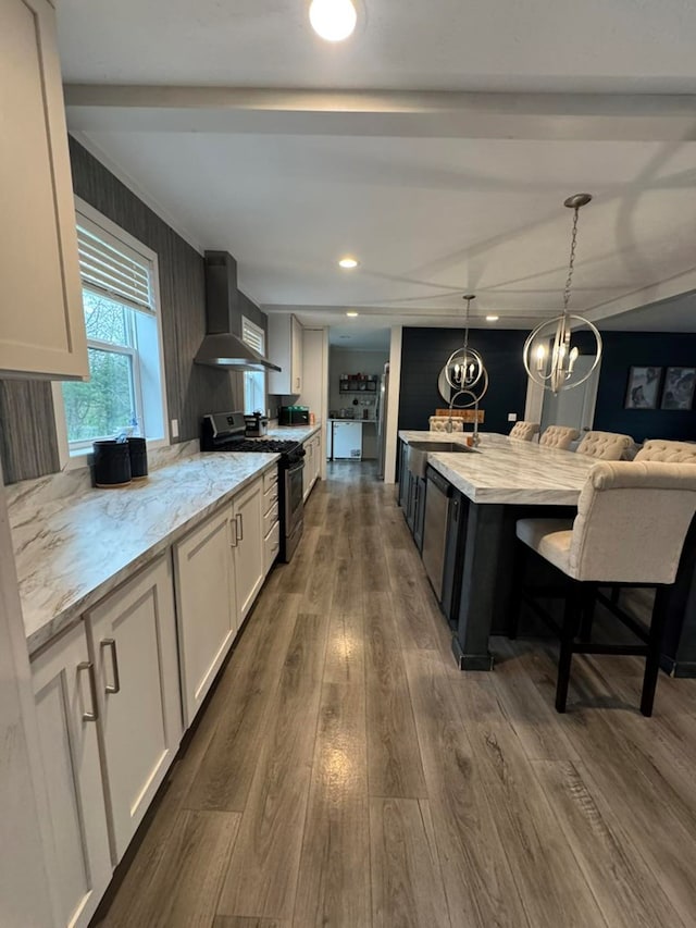 501 SE State St, Milan, MO 63556 - kitchen featuring stainless steel gas stove, wall chimney exhaust hood, white cabinetry, dark wood finished floors, and decorative light fixtures