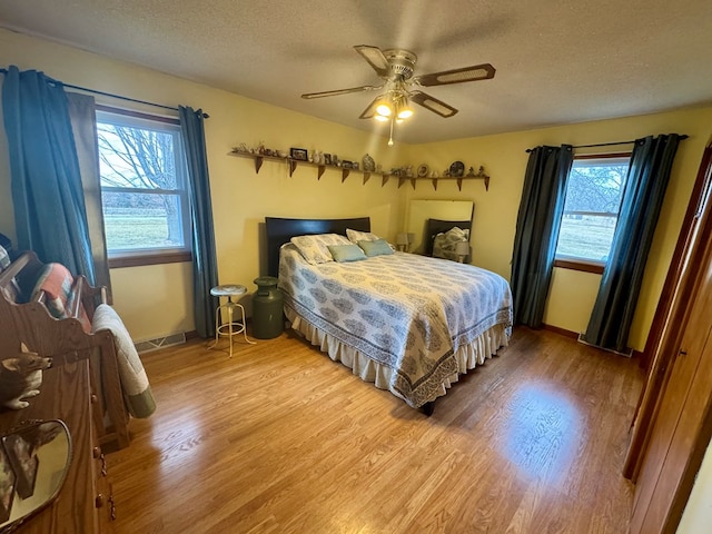 bedroom featuring visible vents, baseboards, ceiling fan, light wood-style flooring, and a textured ceiling