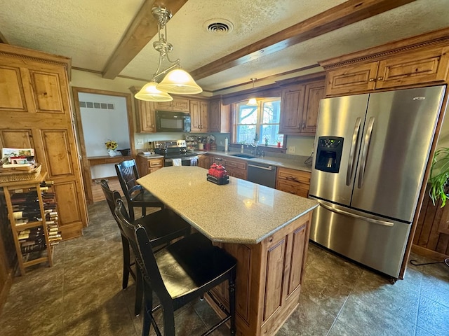 kitchen with a center island, beamed ceiling, brown cabinets, appliances with stainless steel finishes, and a textured ceiling
