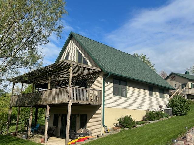 rear view of property with a shingled roof, a patio area, a wooden deck, and a yard