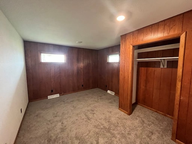 basement with a wealth of natural light, light colored carpet, and wooden walls