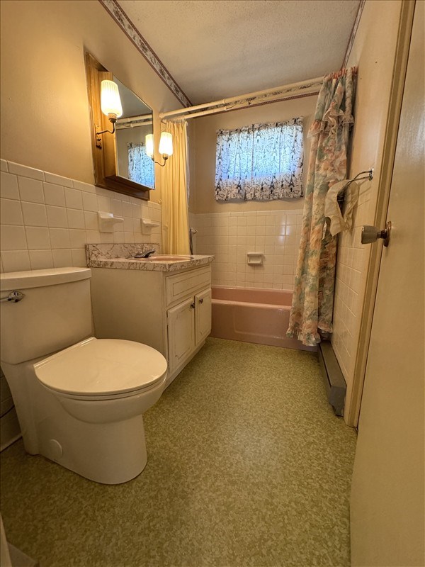 full bathroom featuring a textured ceiling, vanity, shower / bath combo with shower curtain, tile walls, and toilet