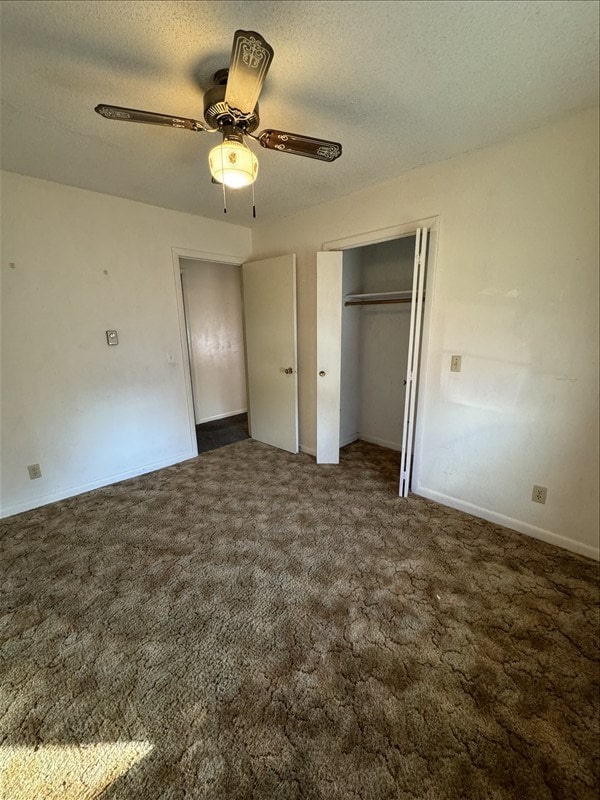 unfurnished bedroom with a textured ceiling, a closet, dark carpet, and ceiling fan