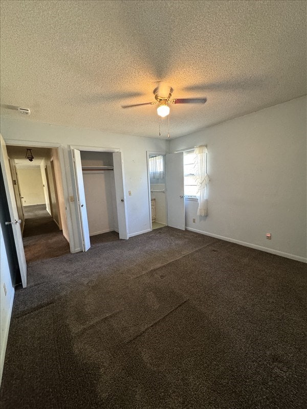 unfurnished bedroom with dark colored carpet, ceiling fan, a textured ceiling, and multiple closets