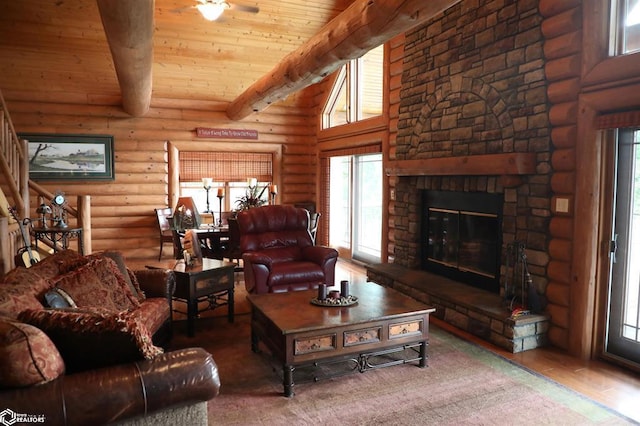 living room with rustic walls, wood finished floors, a high ceiling, a stone fireplace, and beam ceiling