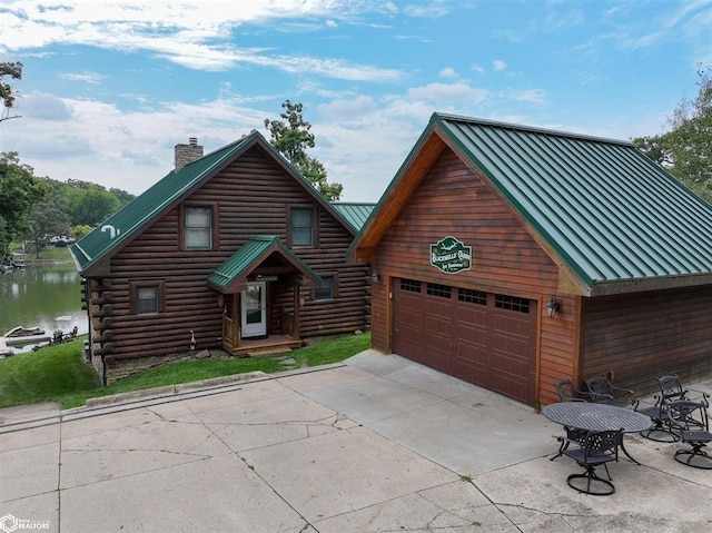 log-style house with a standing seam roof, metal roof, an outbuilding, a water view, and a chimney