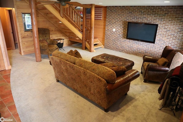 carpeted living area with wood walls, brick wall, stairway, and tile patterned flooring