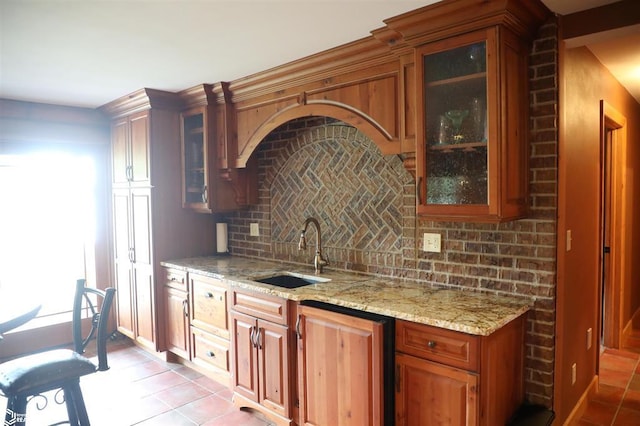 kitchen featuring light stone counters, glass insert cabinets, backsplash, and a sink