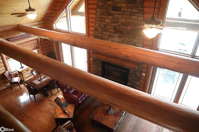 living area featuring a ceiling fan, a stone fireplace, a towering ceiling, and wood finished floors