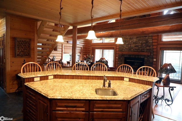 kitchen featuring wooden ceiling, a sink, log walls, an island with sink, and pendant lighting