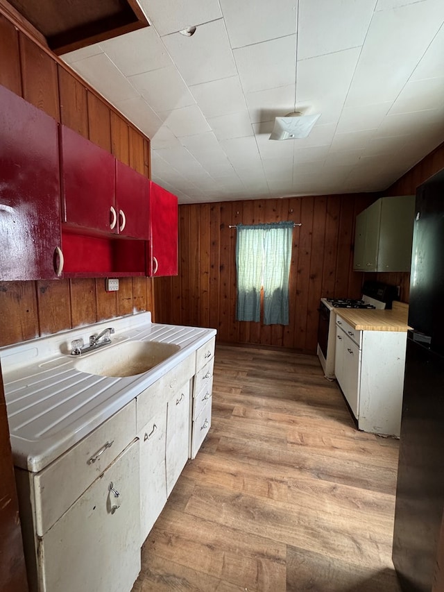 kitchen featuring wooden walls, sink, white gas stove, and light hardwood / wood-style floors