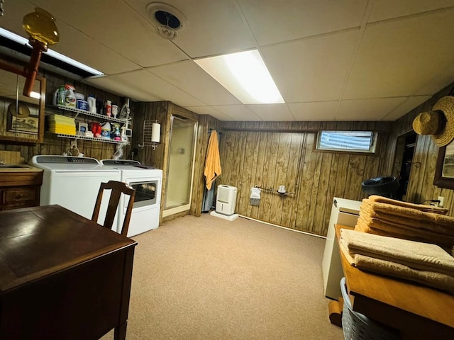 basement with light carpet, a drop ceiling, wood walls, and independent washer and dryer