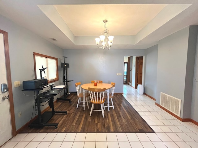 dining area with a tray ceiling, light tile patterned flooring, and a notable chandelier