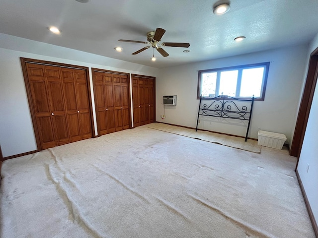 unfurnished bedroom with an AC wall unit, multiple closets, ceiling fan, and light carpet