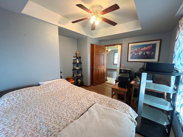 bedroom with ceiling fan, light hardwood / wood-style flooring, and a tray ceiling