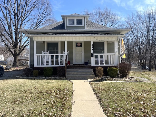 bungalow-style house featuring a porch, a shingled roof, a front lawn, and fence