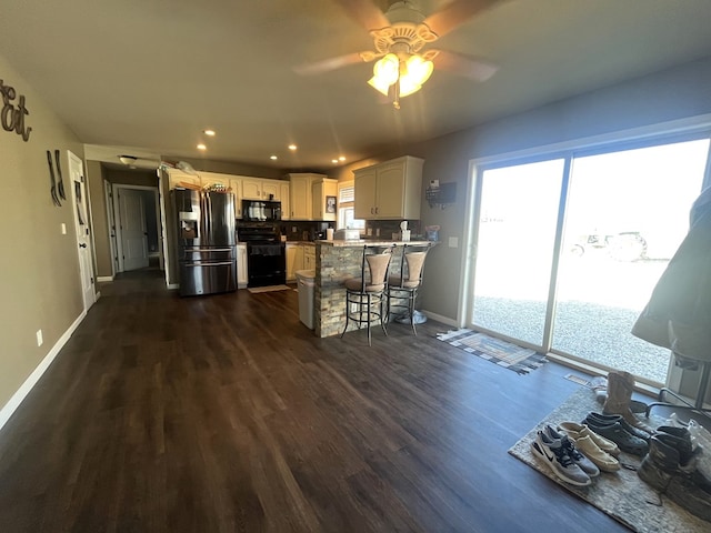 kitchen with dark wood-type flooring, baseboards, a breakfast bar, a peninsula, and black appliances