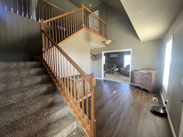 staircase featuring visible vents, a high ceiling, wood finished floors, and baseboards