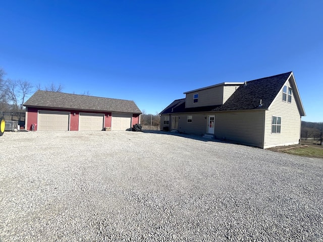 view of side of property featuring an outbuilding, driveway, a garage, and roof with shingles