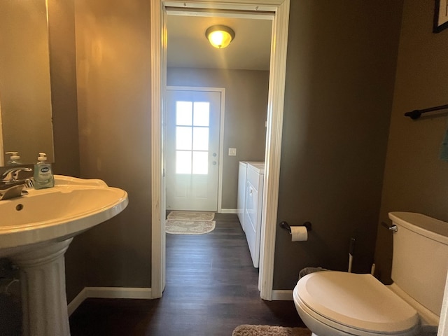 half bathroom with baseboards, toilet, wood finished floors, and washing machine and clothes dryer