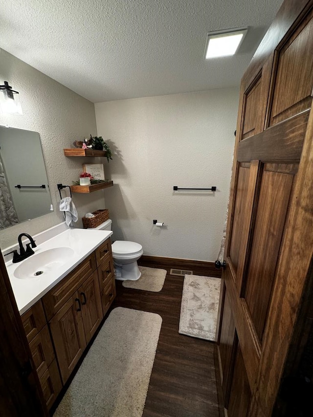 bathroom featuring vanity, a textured ceiling, hardwood / wood-style flooring, and toilet