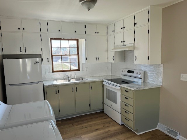 kitchen with under cabinet range hood, white appliances, wood finished floors, a sink, and visible vents