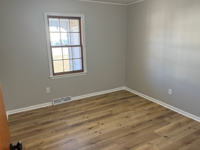 spare room with ornamental molding, wood finished floors, visible vents, and baseboards