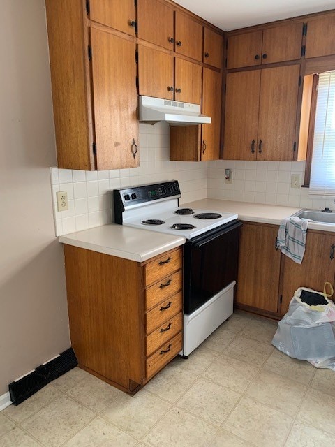 kitchen with brown cabinetry, under cabinet range hood, electric range, and light floors