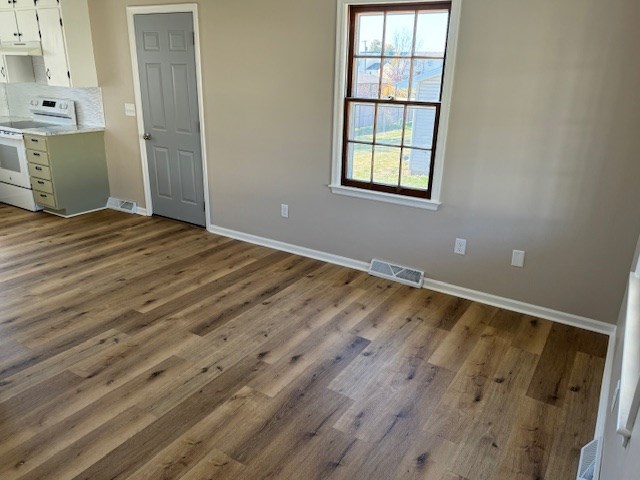 interior space with white electric range oven, visible vents, white cabinetry, wood finished floors, and under cabinet range hood