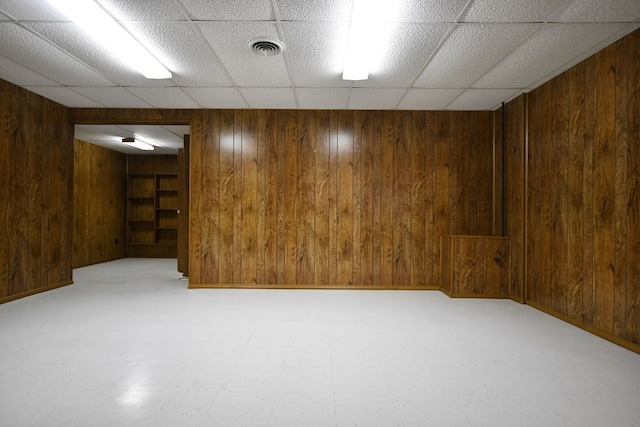 basement featuring a drop ceiling and wood walls