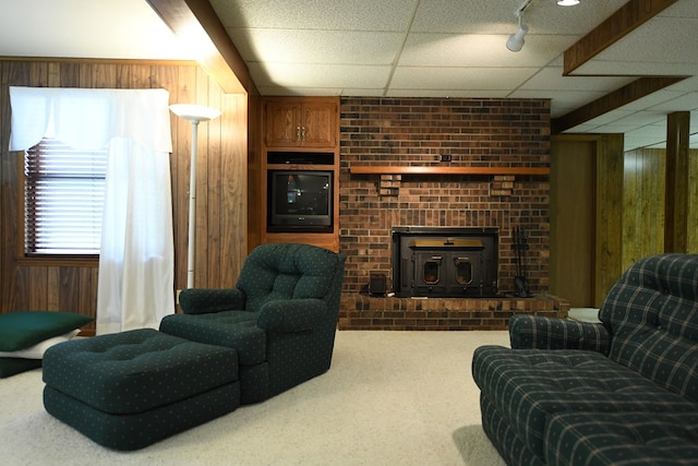 living room with a paneled ceiling, a wood stove, carpet floors, and wooden walls