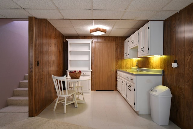 kitchen featuring a paneled ceiling, wood walls, sink, and white cabinets