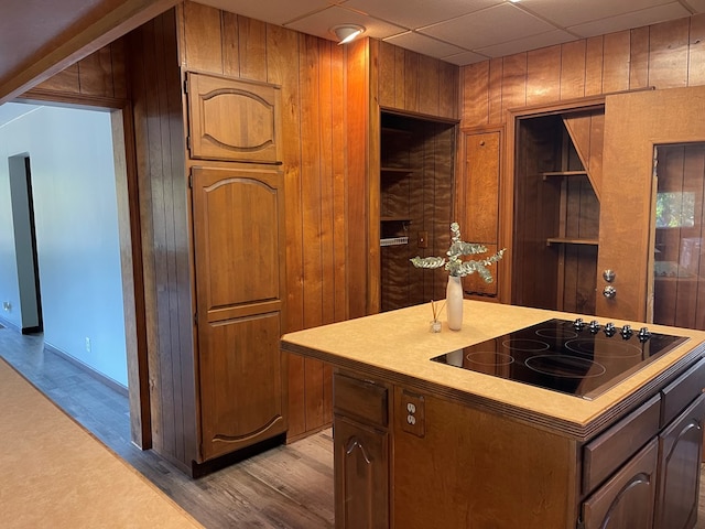 kitchen featuring black electric stovetop, a drop ceiling, wood walls, and light hardwood / wood-style floors