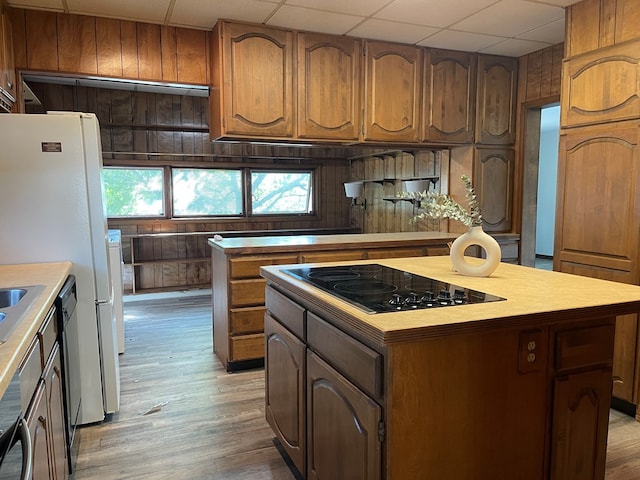 kitchen featuring black electric stovetop, a drop ceiling, wooden walls, light hardwood / wood-style floors, and a kitchen island