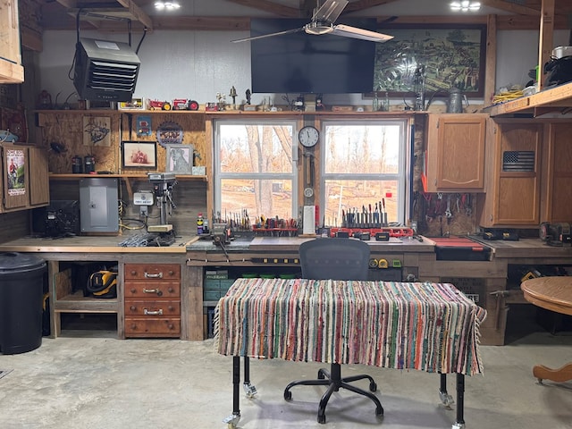 home office featuring ceiling fan, concrete floors, a workshop area, and electric panel