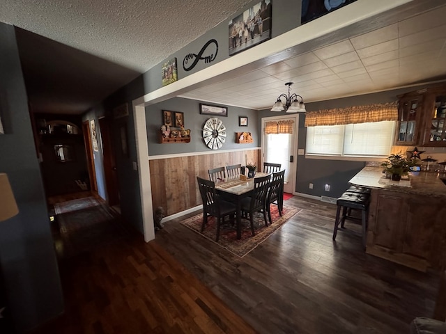 dining space featuring a textured ceiling, a notable chandelier, wooden walls, wainscoting, and dark wood finished floors