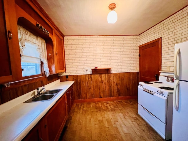 kitchen with white appliances, a wainscoted wall, brick wall, wood finished floors, and a sink