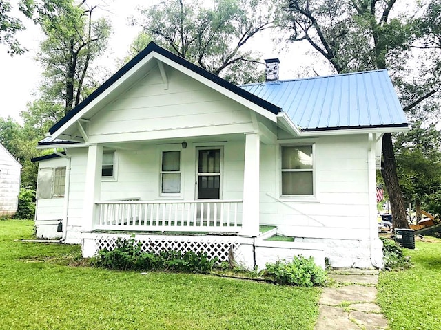 view of front of home featuring metal roof, a chimney, a porch, and a front yard