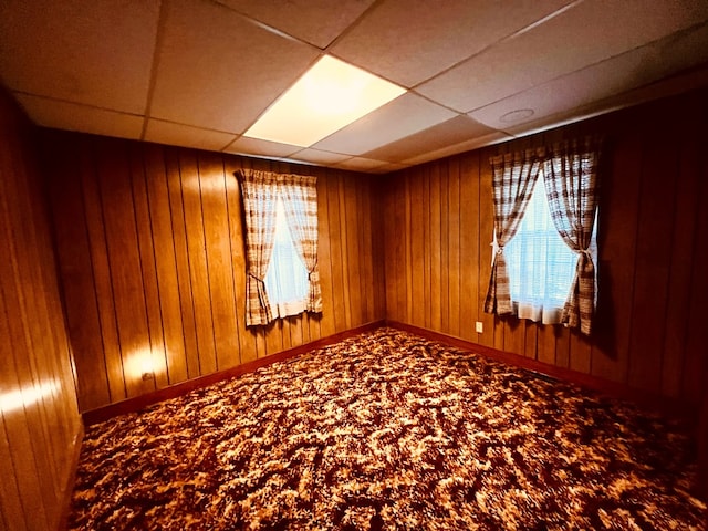 carpeted empty room with baseboards, a paneled ceiling, and wooden walls