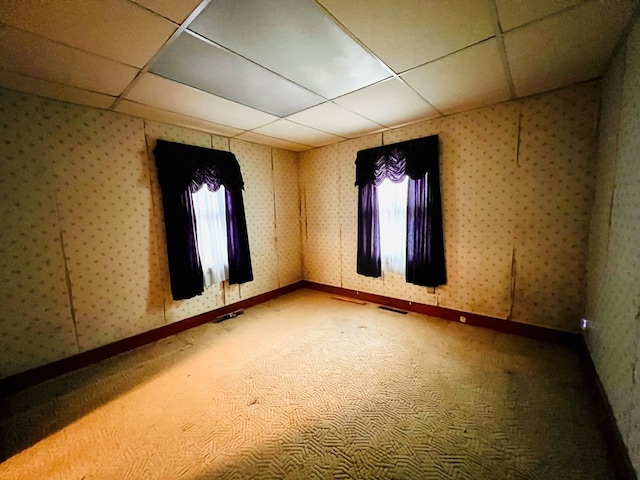 carpeted empty room with wallpapered walls, baseboards, visible vents, and a drop ceiling