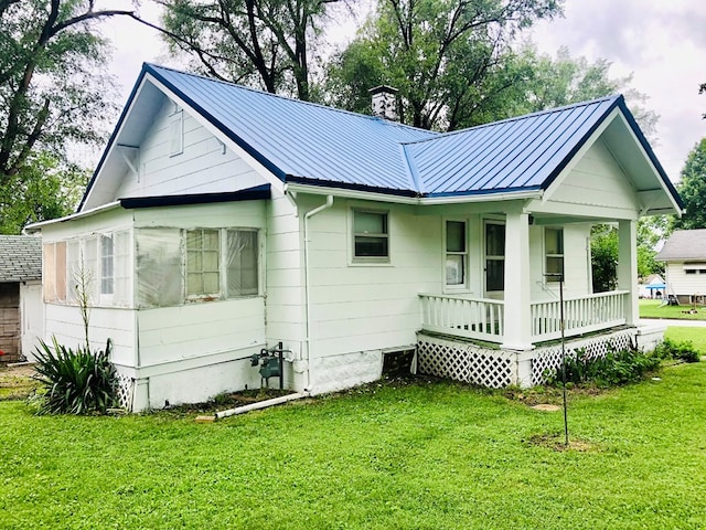 back of property featuring covered porch, a yard, and metal roof