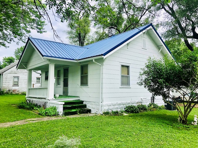 view of side of property featuring a porch, metal roof, a yard, and a chimney