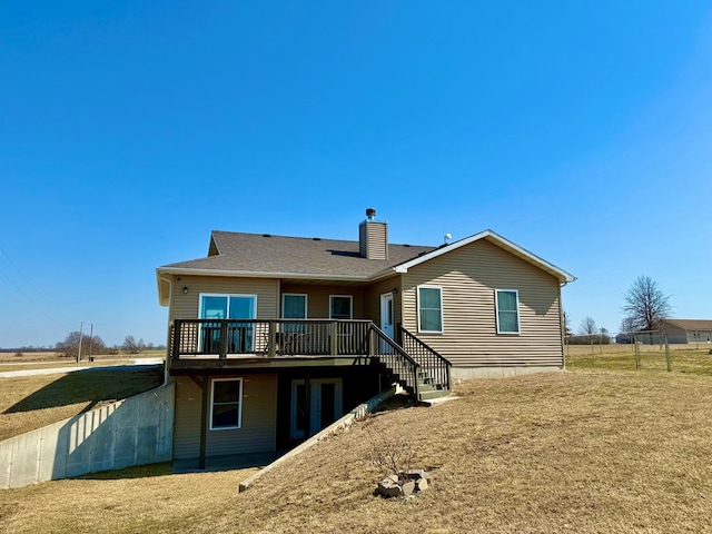 back of property with a deck, a lawn, roof with shingles, and a chimney