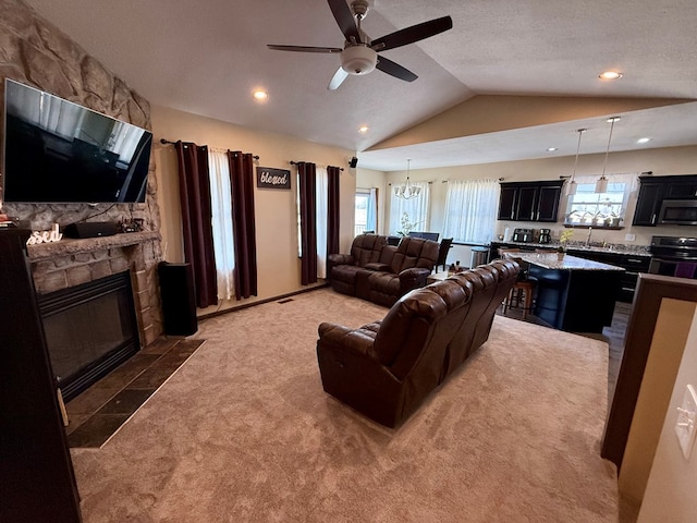 living area featuring a stone fireplace, lofted ceiling, ceiling fan with notable chandelier, and a wealth of natural light