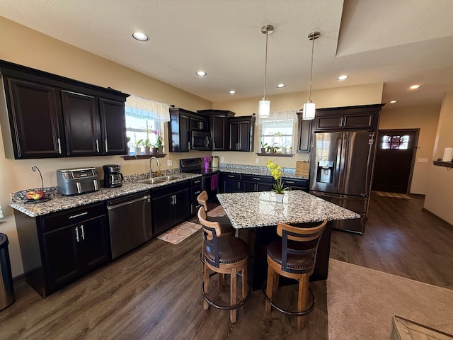 kitchen featuring dark wood finished floors, light stone countertops, appliances with stainless steel finishes, and a sink